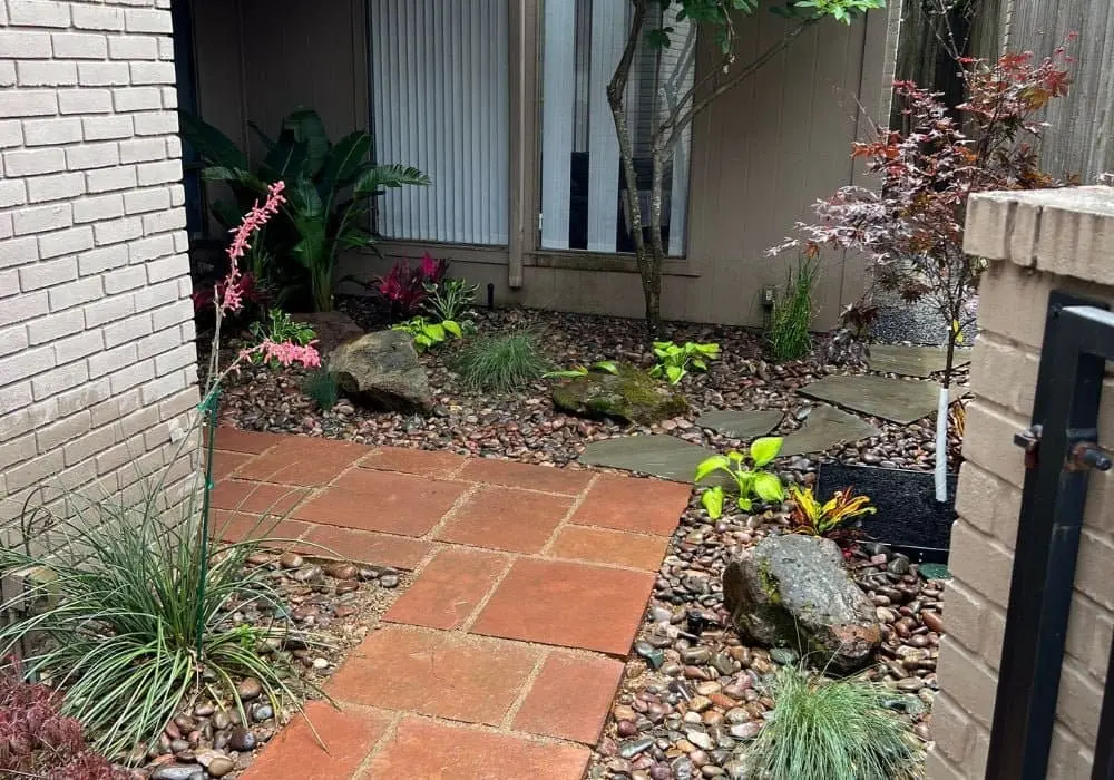 Landscape maintenance in Houston featuring a front courtyard with a blend of tropical and botanical plants, enhanced by decorative river stone and ornamental rock for a natural, elegant look.