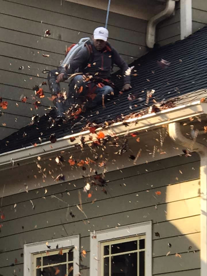 Man using leaf blower to clean gutters of home